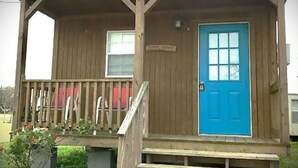 Un bâtiment en bois avec une porte bleue, un petit porche avec des marches et une fenêtre.