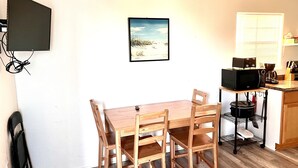 Une petite cuisine avec une table et des chaises en bois, un four à micro-ondes, une machine à café et une fenêtre avec des stores.