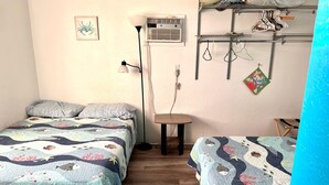 Une chambre avec deux lits, une table de chevet, une lampe, un appareil de climatisation et un portant à vêtements avec des vêtements suspendus.