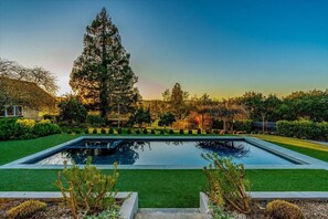A rectangular swimming pool with a surrounding green lawn and a tall tree in the background. - Eastside Eden - Pool, Hot Tub and Tastings Included (Healdsburg)