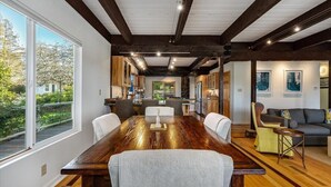 A spacious dining area with a long wooden table, surrounded by chairs, and a view of a garden through large windows. - Eastside Eden - Pool, Hot Tub and Tastings Included (Healdsburg)