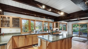 A spacious kitchen with wooden cabinets, a large island, and large windows. - Eastside Eden - Pool, Hot Tub and Tastings Included (Healdsburg)