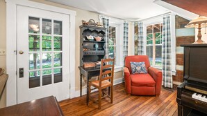 A room with a wooden floor, a red armchair, a bookshelf, a piano, and a door with a window. - Historical 52 acres, Brown County, Pets (Nashville)