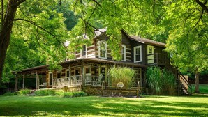 A log cabin with a porch, surrounded by lush greenery and trees. - Historical 52 acres, Brown County, Pets (Nashville)