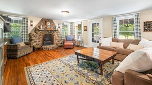 A cozy living room with a stone fireplace, wooden flooring, and a large window with plaid curtains. - Historical 52 acres, Brown County, Pets (Nashville)