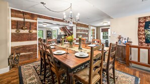 A dining room with a wooden table set for six, surrounded by wooden chairs. A chandelier hangs from the ceiling, and a wooden staircase is visible in the background. - Historical 52 acres, Brown County, Pets (Nashville)