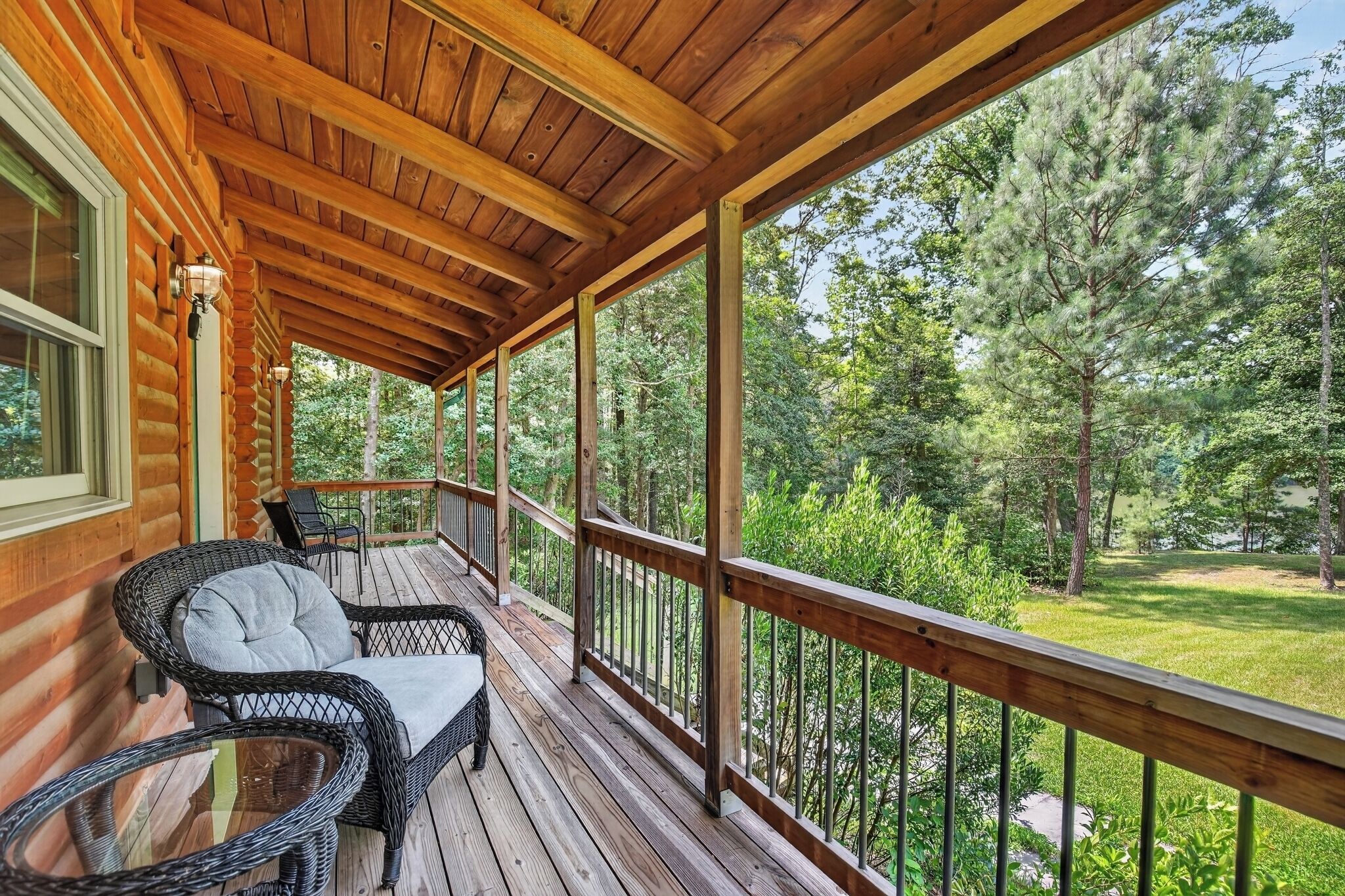 Une terrasse en bois, meublée de meubles en osier, avec vue sur une zone boisée.