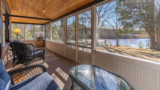 A covered patio with wicker furniture, a glass table, and a view of a lake.
