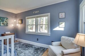 A room with a large window, a white sofa, a lamp, and a small table with a lamp. - Pizza Friday (Ridge)