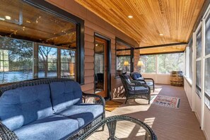 A covered outdoor seating area with wicker furniture and large windows.
