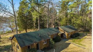A cabin with a green roof, surrounded by trees and a grassy area.