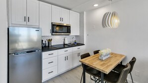A modern kitchen with white cabinets, stainless steel appliances, and a wooden dining table with chairs. - Ocean Front 1 Bed renovated in Daytona Beach (Daytona Beach)
