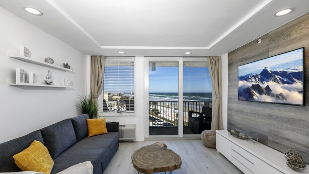 A modern living room with a gray sofa, a round wooden coffee table, and a large flat-screen TV mounted on a wooden wall. - Ocean Front 1 Bed renovated in Daytona Beach (Daytona Beach)