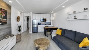 A modern kitchen with white cabinets, a stainless steel refrigerator, and a dining area with a gray sofa and yellow pillows. - Ocean Front 1 Bed renovated in Daytona Beach (Daytona Beach)