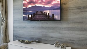 A modern living room with a large flat-screen TV mounted on a wooden wall, a white console table with decorative items, and a light-colored floor. - Ocean Front 1 Bed renovated in Daytona Beach (Daytona Beach)