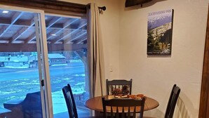 Uma área de refeições com mesa e cadeiras, um cartaz na parede e vista através de uma porta de vidro.