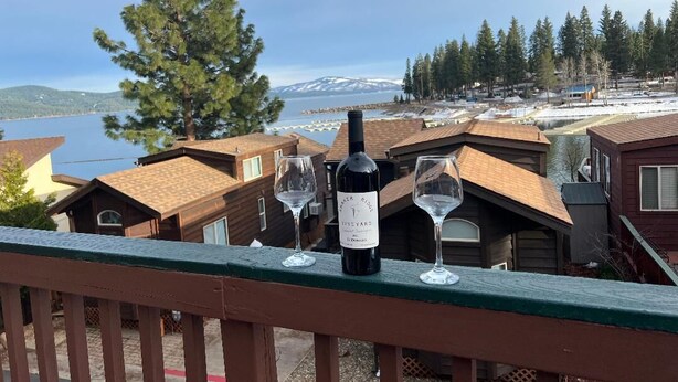 Un balcón con una botella de vino y dos copas, con vistas a un lago y un paisaje nevado.