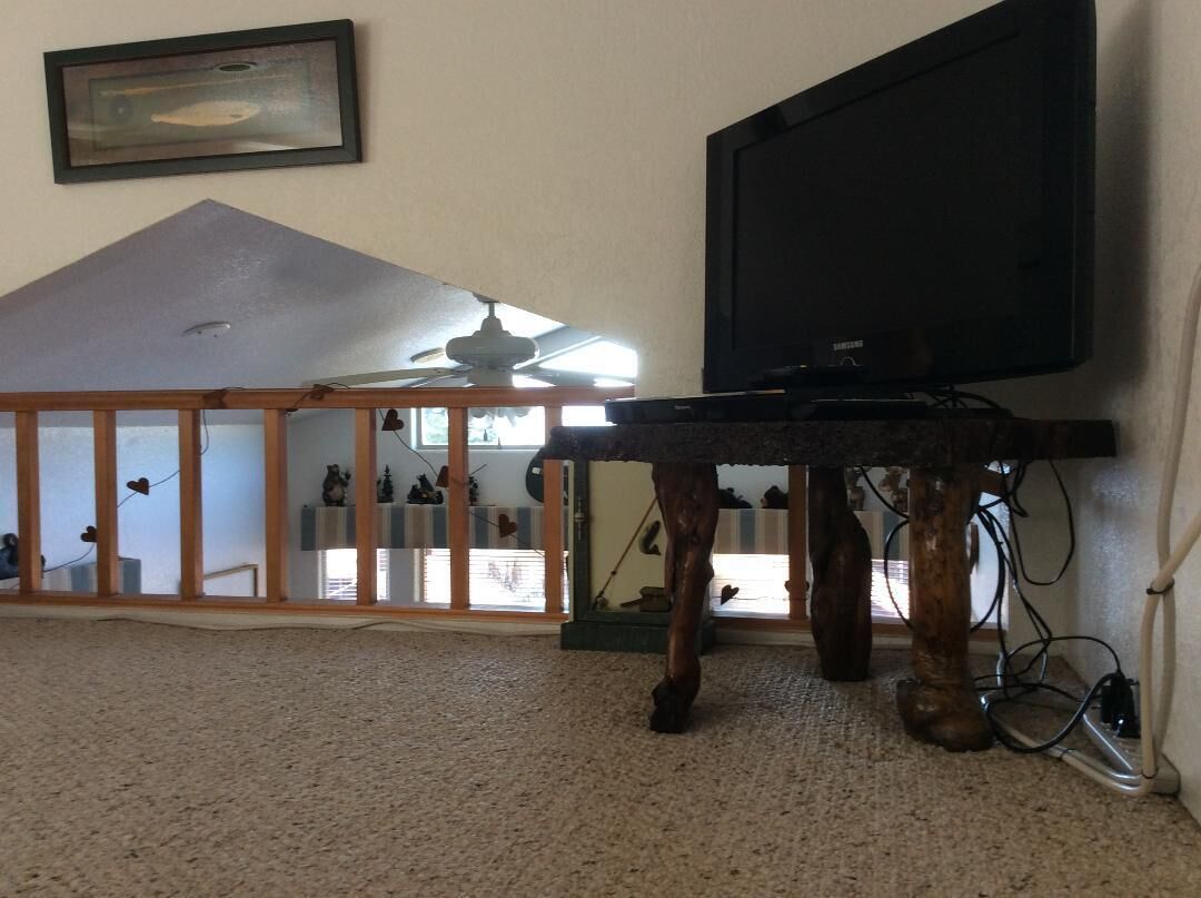 A room with a television on a wooden stand, a ceiling fan, and a view of a balcony with a railing.