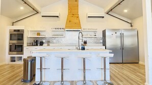 A modern kitchen with a central island, stainless steel appliances, and a wooden staircase.