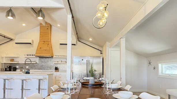 A modern dining area with a long wooden table set for a meal, surrounded by white chairs.