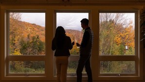 A room with three large windows offering a view of autumn foliage.