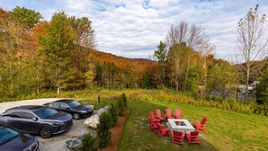 A parking area with several cars, a grassy lawn, and a fire pit with red chairs.