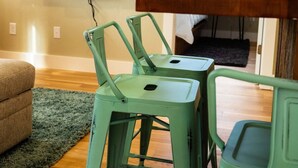 A living room with two green metal chairs, a wooden table, a flat-screen TV mounted on the wall, and a sofa. - Charming Downtown Cody Cottage (#1) (Cody)