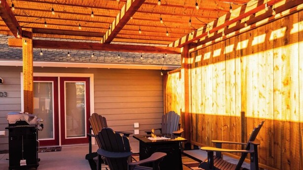 An outdoor patio with wooden flooring, a table, chairs, and a grill. - Charming Downtown Cody Cottage (#1) (Cody)