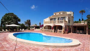 Una casa de dos pisos con piscina, mobiliario exterior y un balcón.