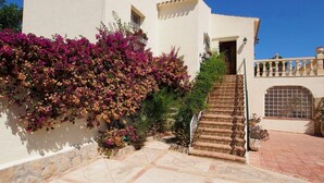 Un edificio con una escalera que conduce a una puerta, rodeado por un jardín con flores moradas.
