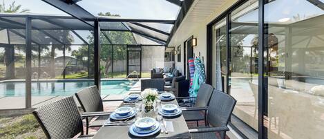 A covered patio with a table set for dining, overlooking a swimming pool.