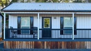 A small, single-story building with a porch, a wooden deck, and a metal roof. - Charming Cabin Retreat in Texas Hill Country (Boerne)