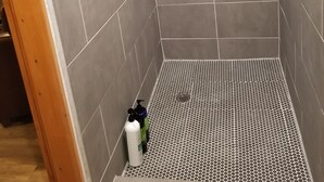 A shower with grey tiles, a showerhead, and a drainage grate.