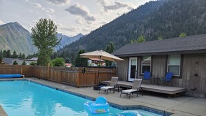 A backyard with a swimming pool, lounge chairs, and a wooden deck.