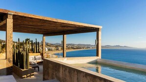 A poolside area with a wooden pergola, seating, and a view of the sea and cityscape. - Private Hot Tub • Ocean View • GYM • Free Parking (San José del Cabo)
