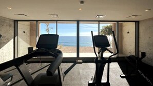 A gym with two exercise bikes facing a large window overlooking a beach. - Private Hot Tub • Ocean View • GYM • Free Parking (San José del Cabo)