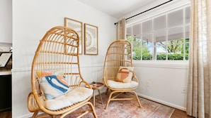A room with two wicker chairs, a patterned rug, and a large window with curtains. - The Gathering Place - Boho Getaway Perfect For Family Stays! (Lubbock)