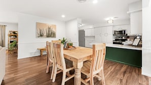 A modern kitchen with white cabinets, a wooden dining table, and a green island. - The Gathering Place - Boho Getaway Perfect For Family Stays! (Lubbock)