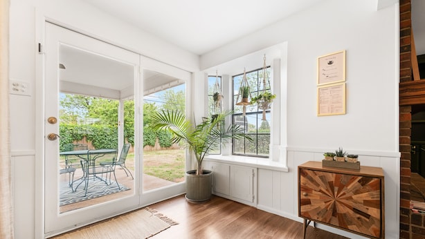 A room with a sliding glass door leading to an outdoor patio, a wooden cabinet with a geometric design, and a potted plant. - The Gathering Place - Boho Getaway Perfect For Family Stays! (Lubbock)