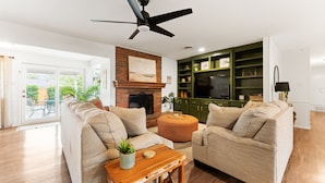 A modern living room with a fireplace, green shelving, and a ceiling fan. - The Gathering Place - Boho Getaway Perfect For Family Stays! (Lubbock)