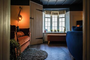 A cozy living room with a sofa, a blue armchair, a wooden door, and a window with blinds.