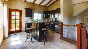 A kitchen with a wooden ceiling, a large island with stools, dark cabinets, and stainless steel appliances. - Casa de Amigos, Island Townhome (Placencia)