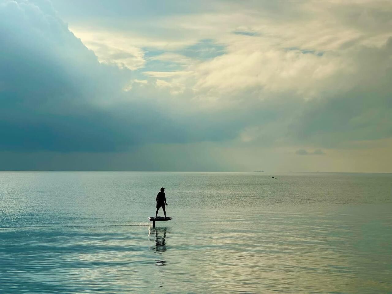 A person paddleboarding on a calm sea under a cloudy sky.