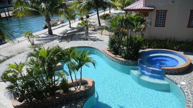 A pool area with a small hot tub, surrounded by palm trees and a stone deck. - Casa de Amigos, Island Townhome (Placencia)