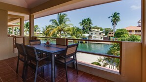A balcony with a table and chairs overlooking a pool and palm trees. - Casa de Amigos, Island Townhome (Placencia)