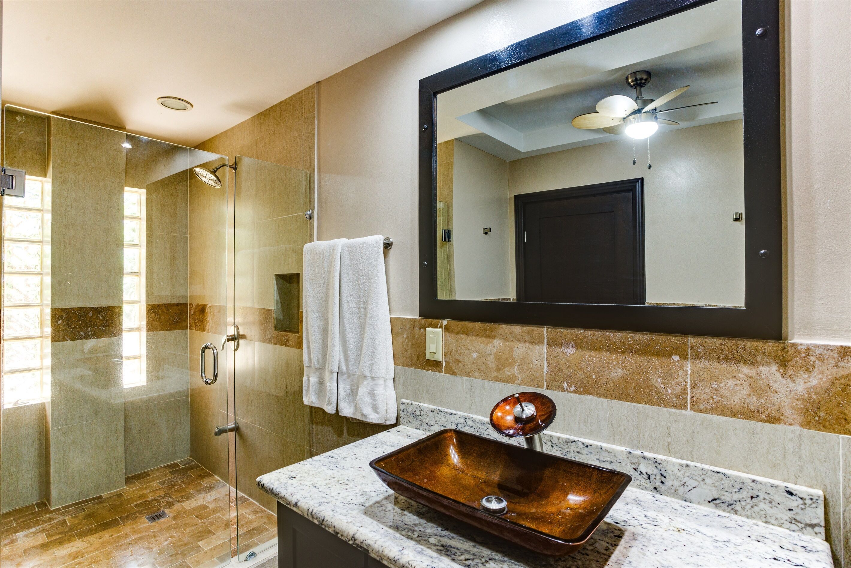 A modern bathroom with a glass-enclosed shower, a vessel sink, and a large mirror above the sink.