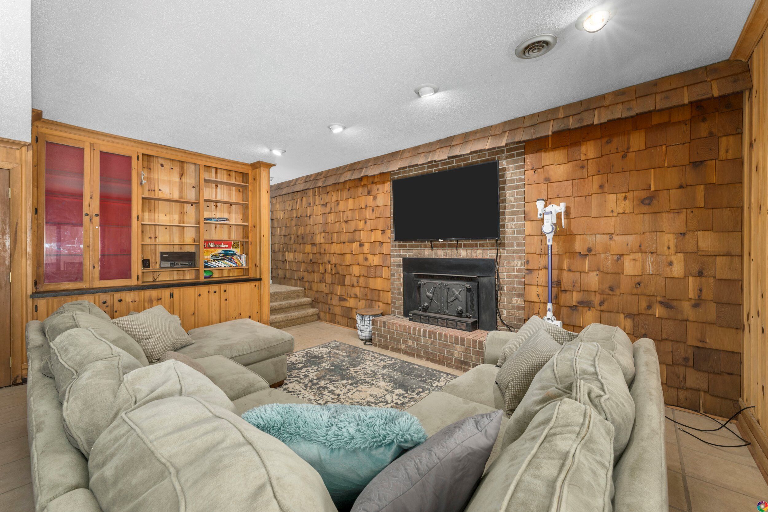 Un salon chaleureux avec une cheminée, des murs en bois et un grand téléviseur à écran plat fixé au-dessus.