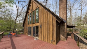 A wooden cabin with a deck, large windows, and a chimney.