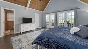 A bedroom with a large bed, a television on a dresser, and a view of the outdoors through a sliding glass door.