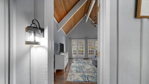 A hallway leading to a room with a wooden ceiling, a white wall, and a blue patterned rug.